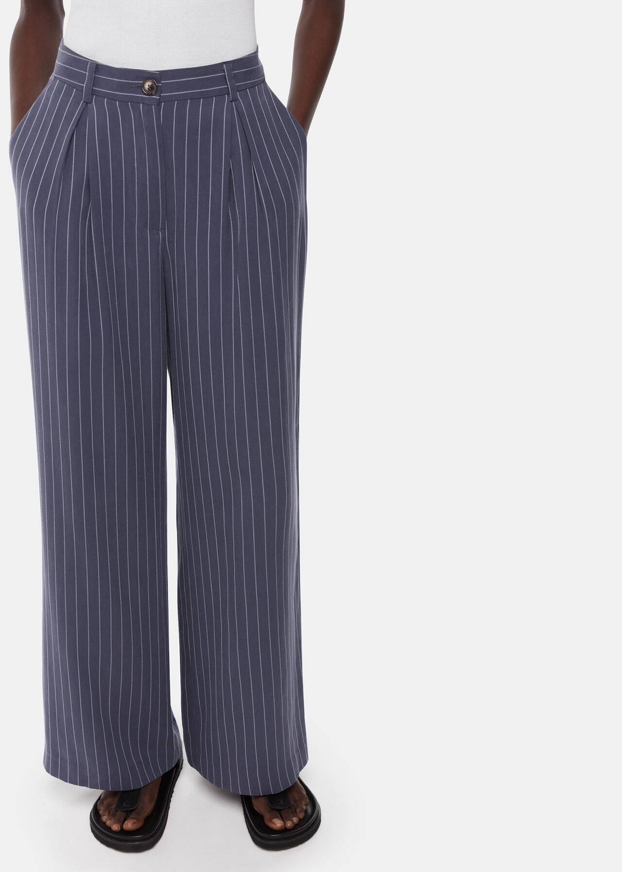 A pair of navy pinstripe trousers with pleats and side pockets, worn by a woman.