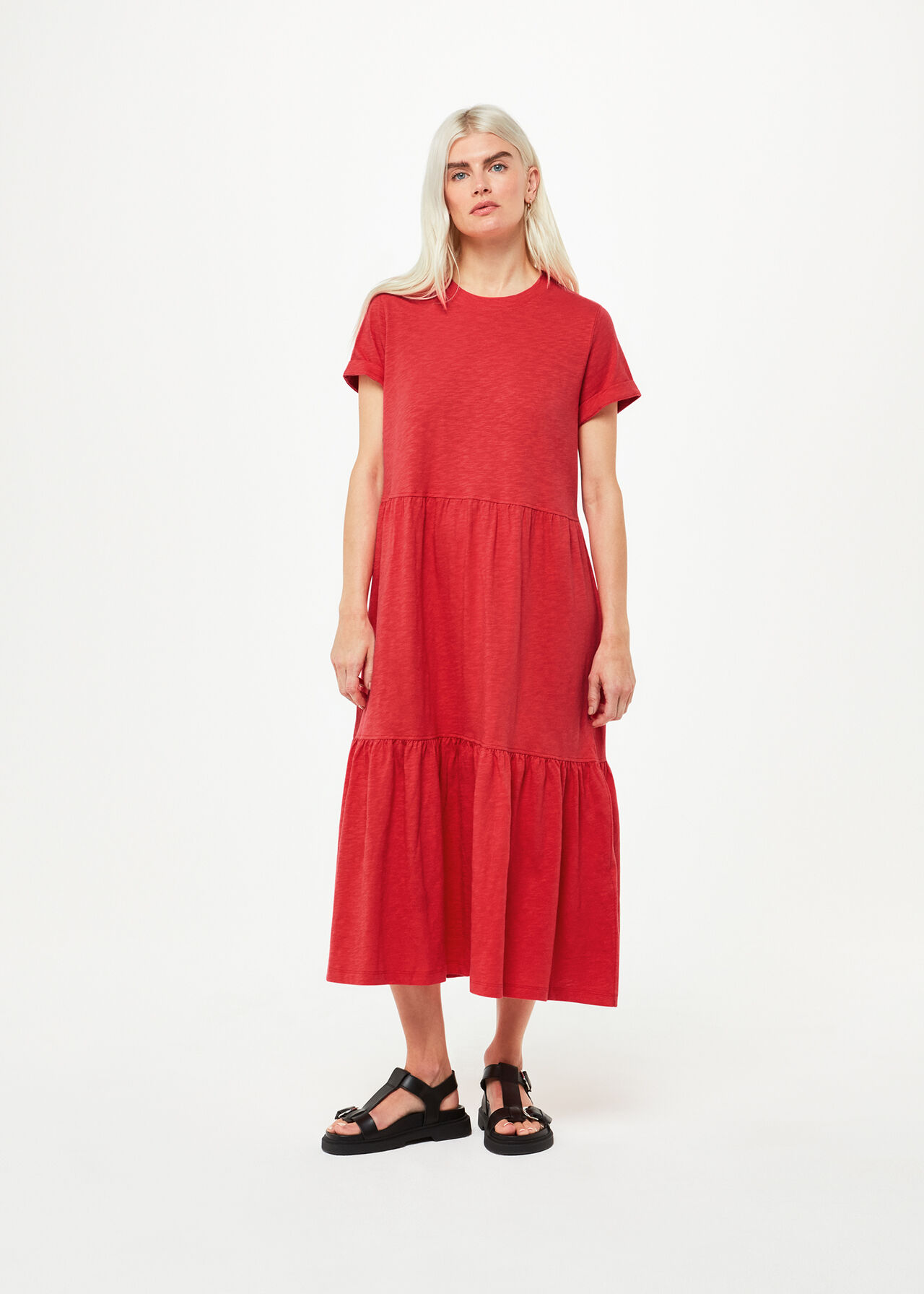 A woman wearing a red midi dress with tiered layers, short sleeves, and a relaxed fit, paired with black sandals.