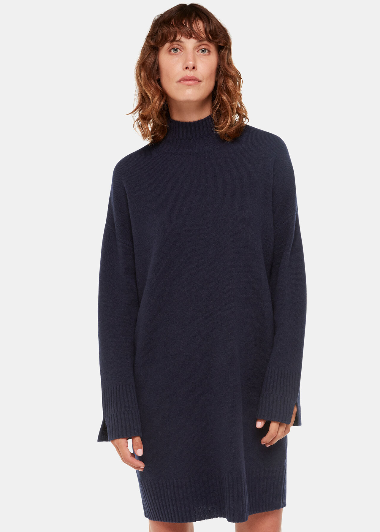 A woman wearing a navy knitted dress with a funnel neck and long sleeves, standing against a plain background.