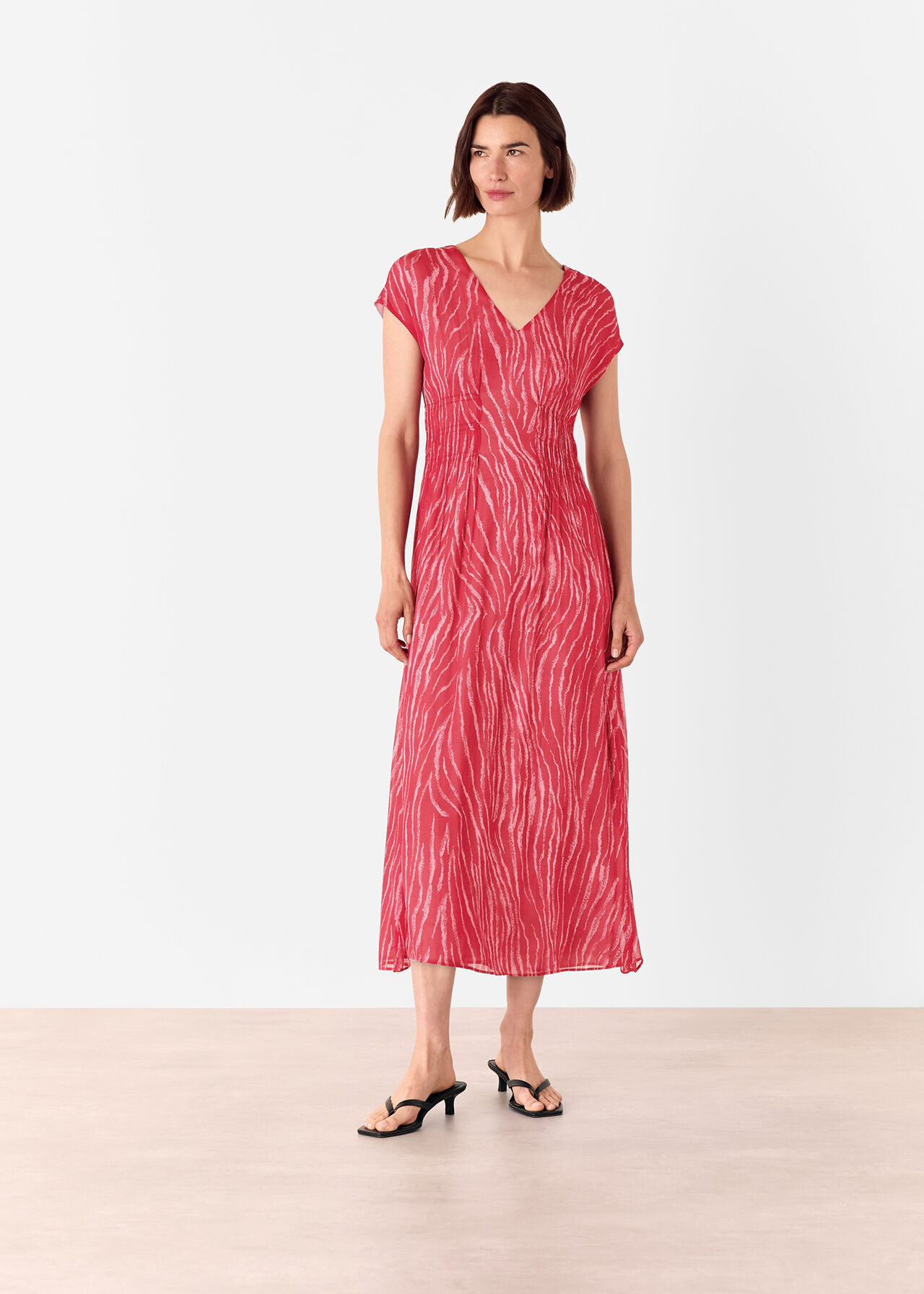 A woman wearing a red midi dress with zebra pattern, V-neckline, short sleeves, and a textured fabric.