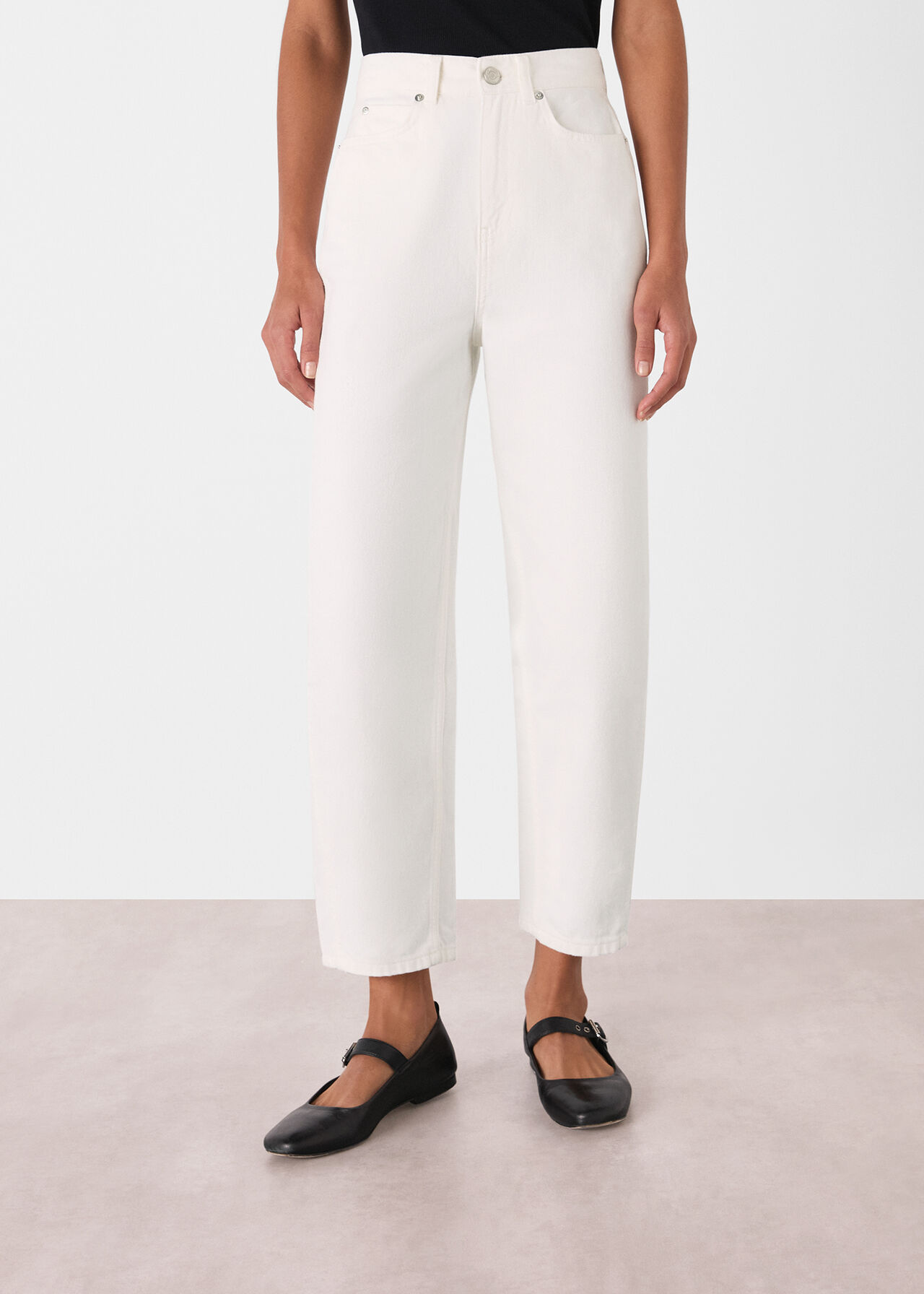 A woman wearing white high-rise barrel leg jeans with a black top and black shoes.