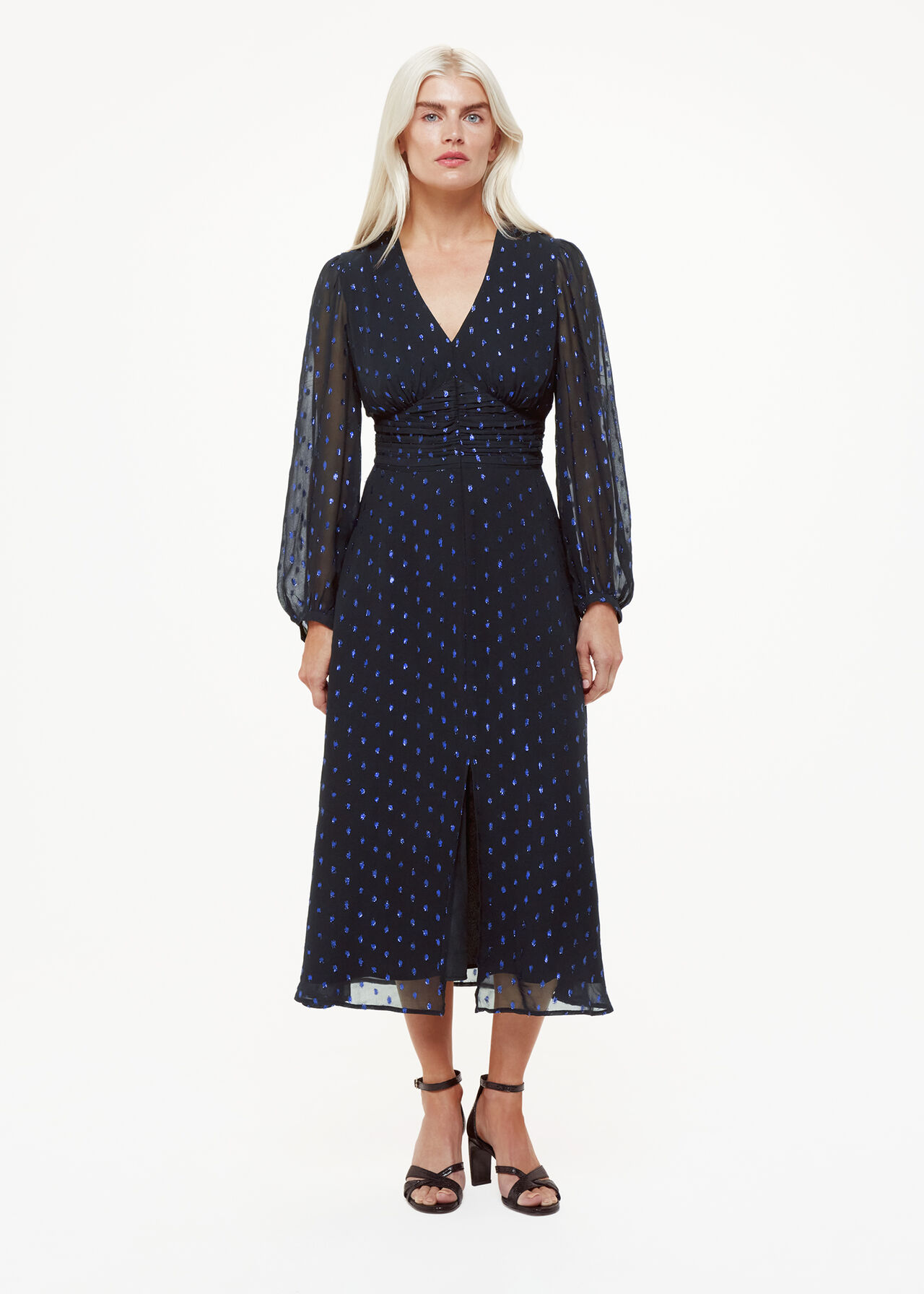A woman wearing a navy midi dress with sheer long sleeves, a V-neckline with ruffle details, and a fitted waist, featuring metallic dot prints.