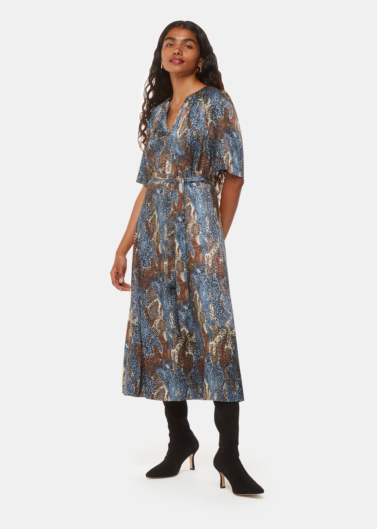 A woman wearing a dress with a short-sleeve silhouette, V-neckline, and a waist-cinching belt, featuring an abstract spot print in blue hues.