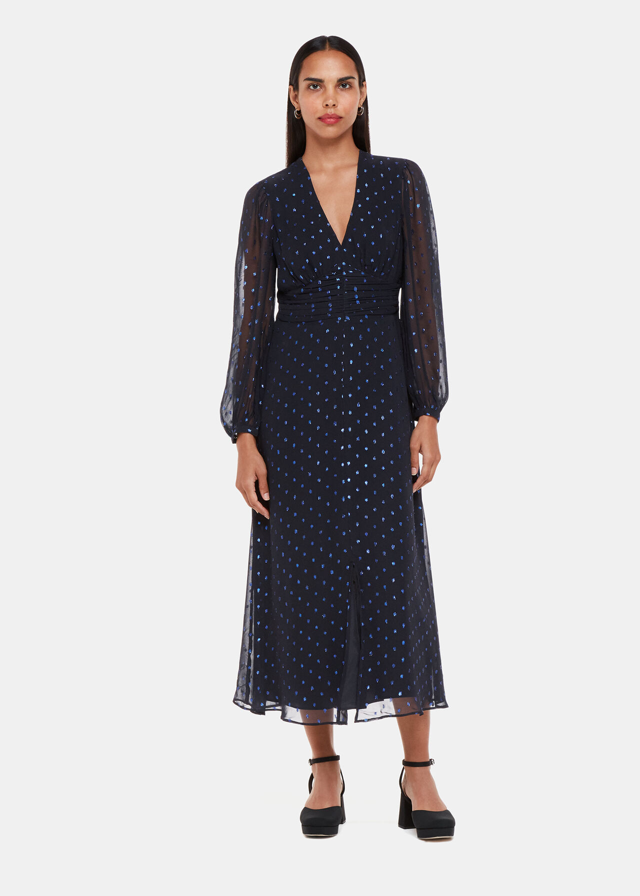 A woman wearing a navy metallic dobby midi dress with a V-neck, long sheer sleeves, and a fitted waist, featuring shimmery dot prints.