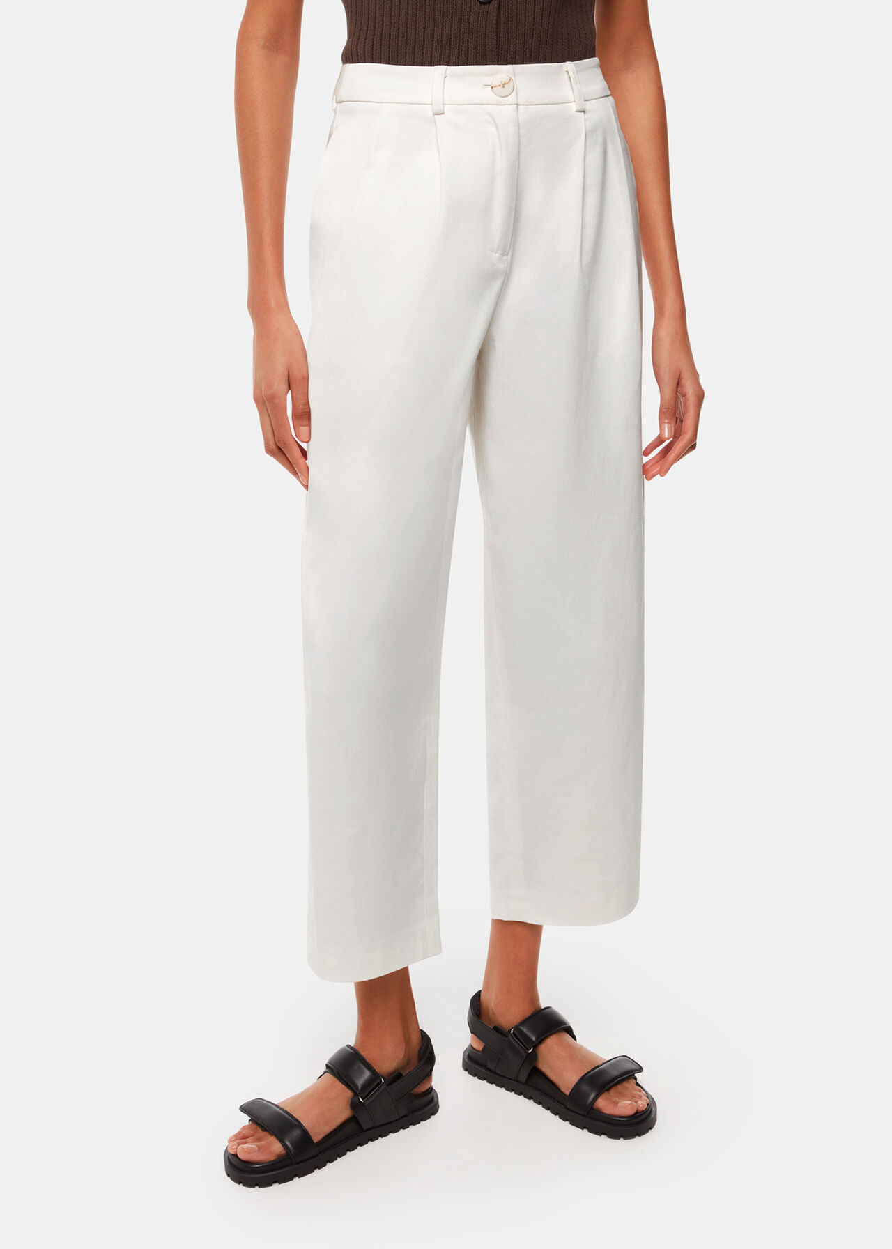 A pair of white women's trousers with a high waist, front pleats, and a barrel leg style, worn with black sandals.