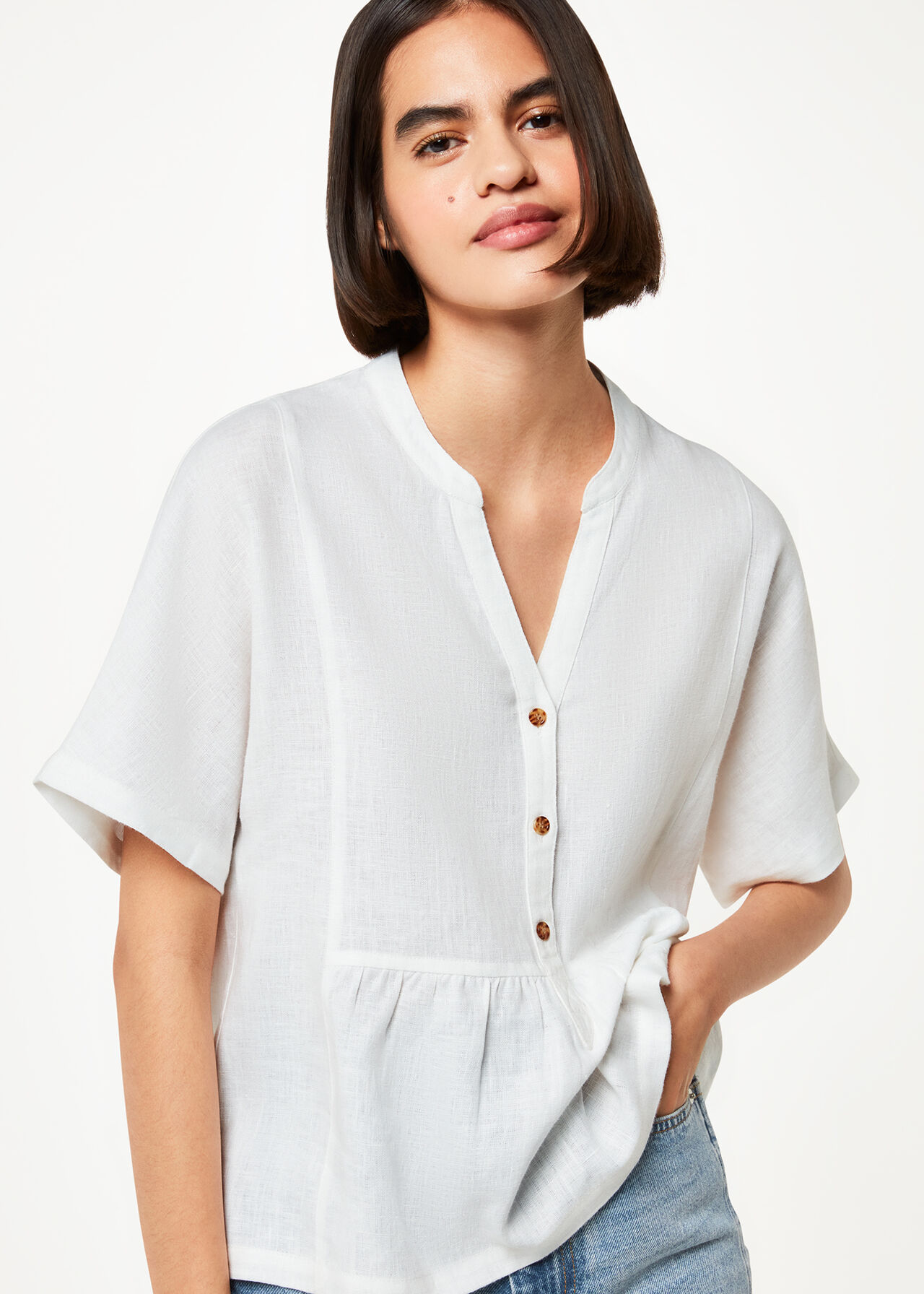 A woman wearing a white linen blouse with a V-neck, button closure, and elbow-length sleeves.