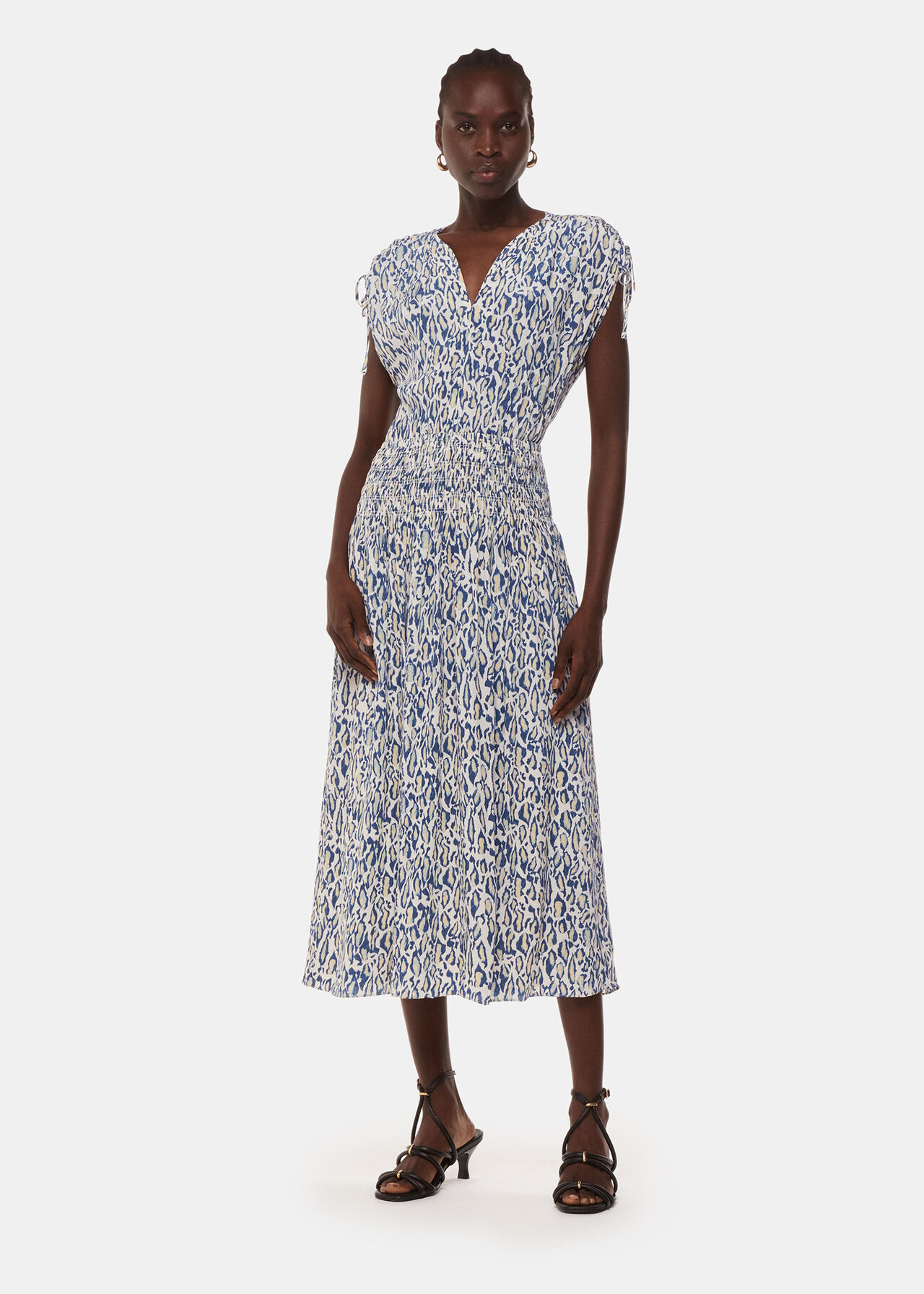 A woman wearing a midi dress with a blue and beige flaming leopard print, V-neckline, tie shoulders, and cinched waist.