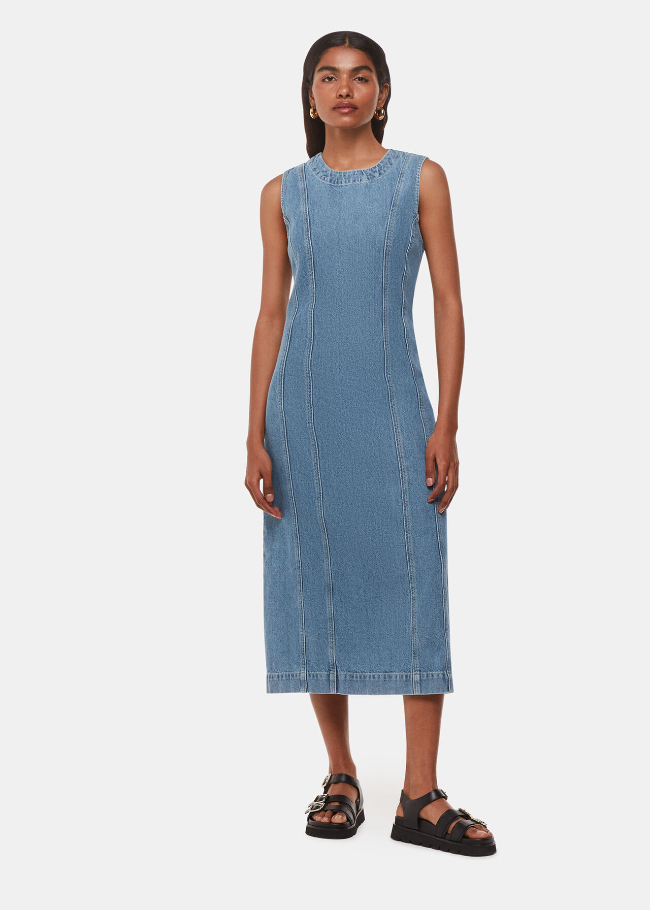 A woman wearing a sleeveless blue denim midi dress with a straight silhouette, standing against a plain background.