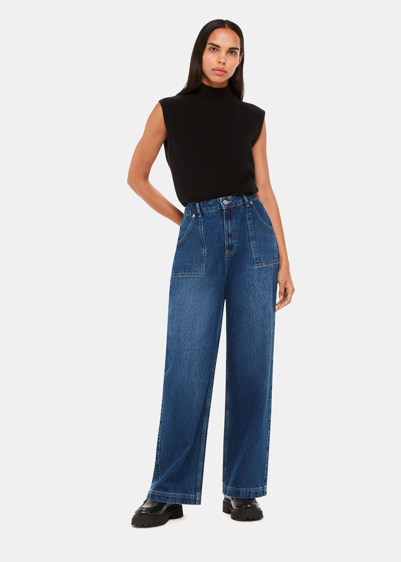 A woman wearing high-waisted, mid wash denim straight-leg jeans with large front pockets, paired with a black sleeveless turtleneck top.