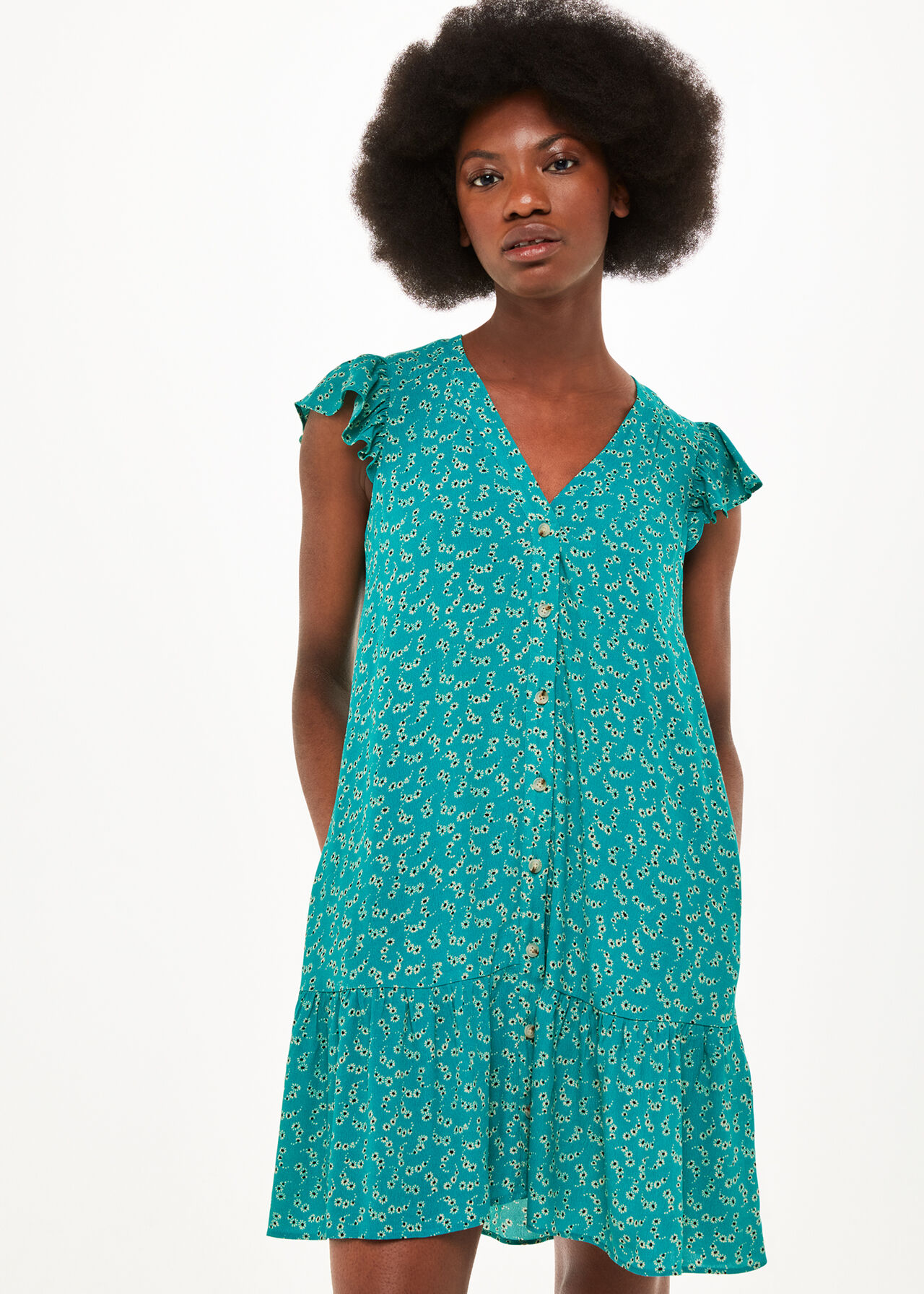 A woman wearing a teal dress with a floral pattern, short puff sleeves, button front, and a tiered hem.