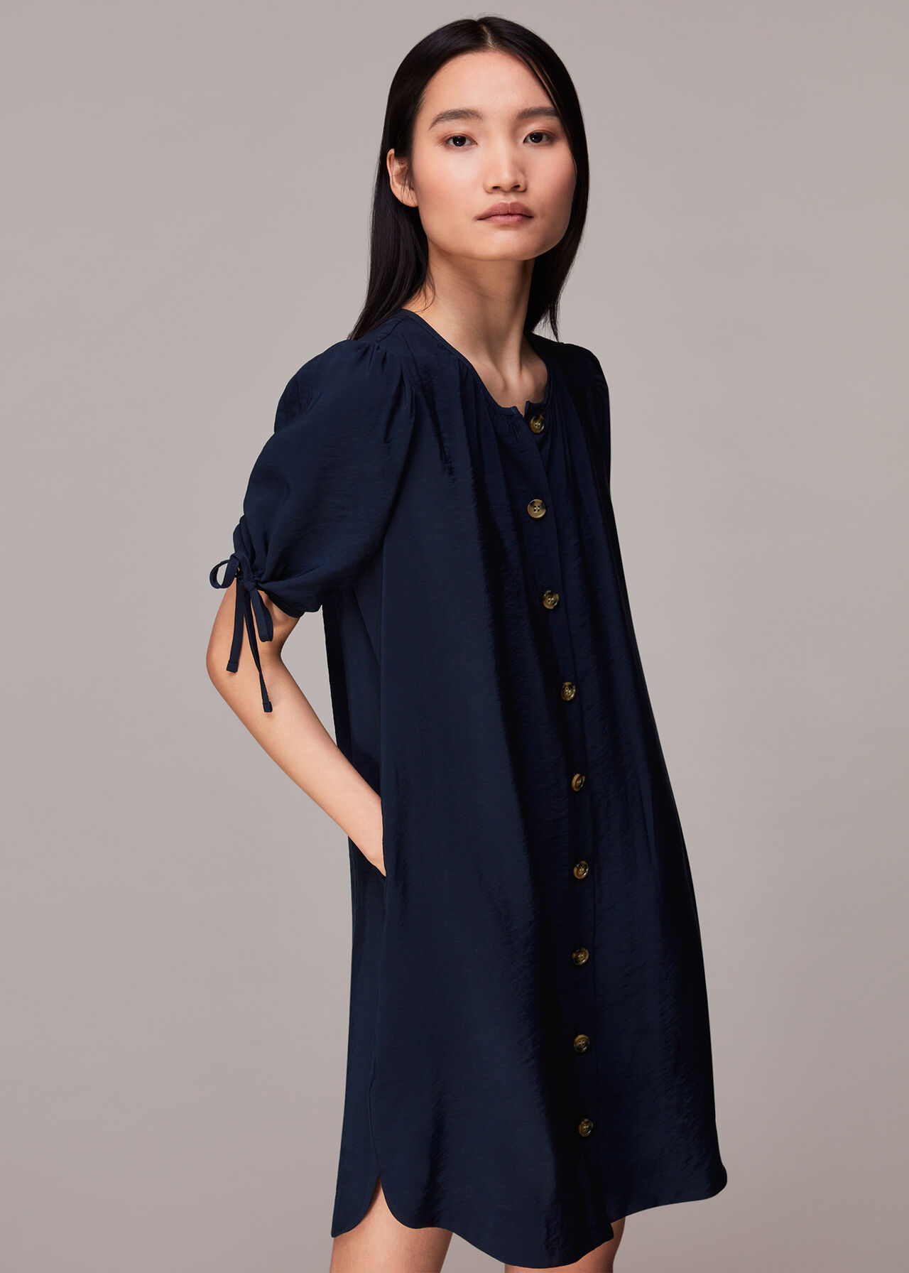 A woman wearing a navy button-through dress with a relaxed fit, button details down the front, and tied sleeves.