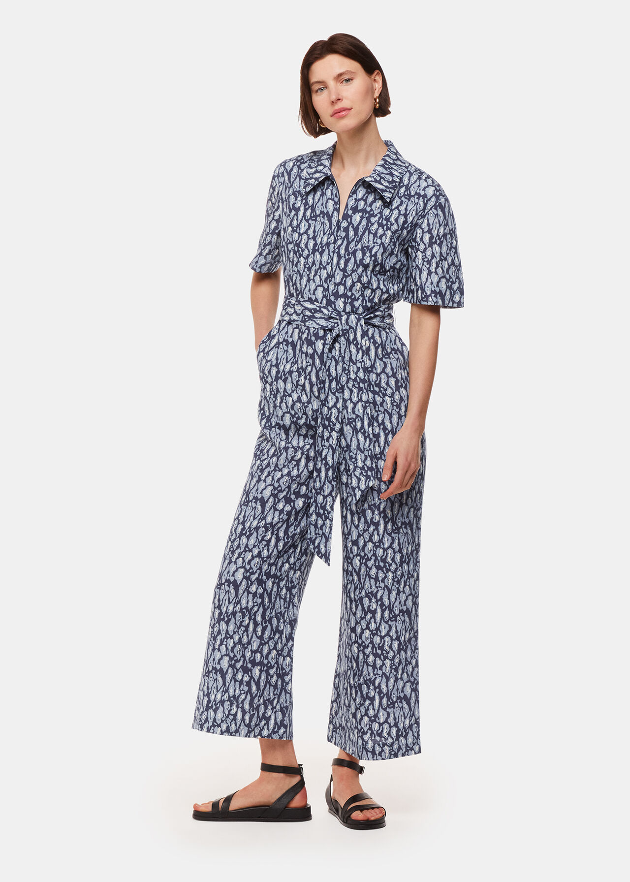 A woman wearing a leopard print linen blend jumpsuit with a collared neckline, short sleeves, and a fitted waist.