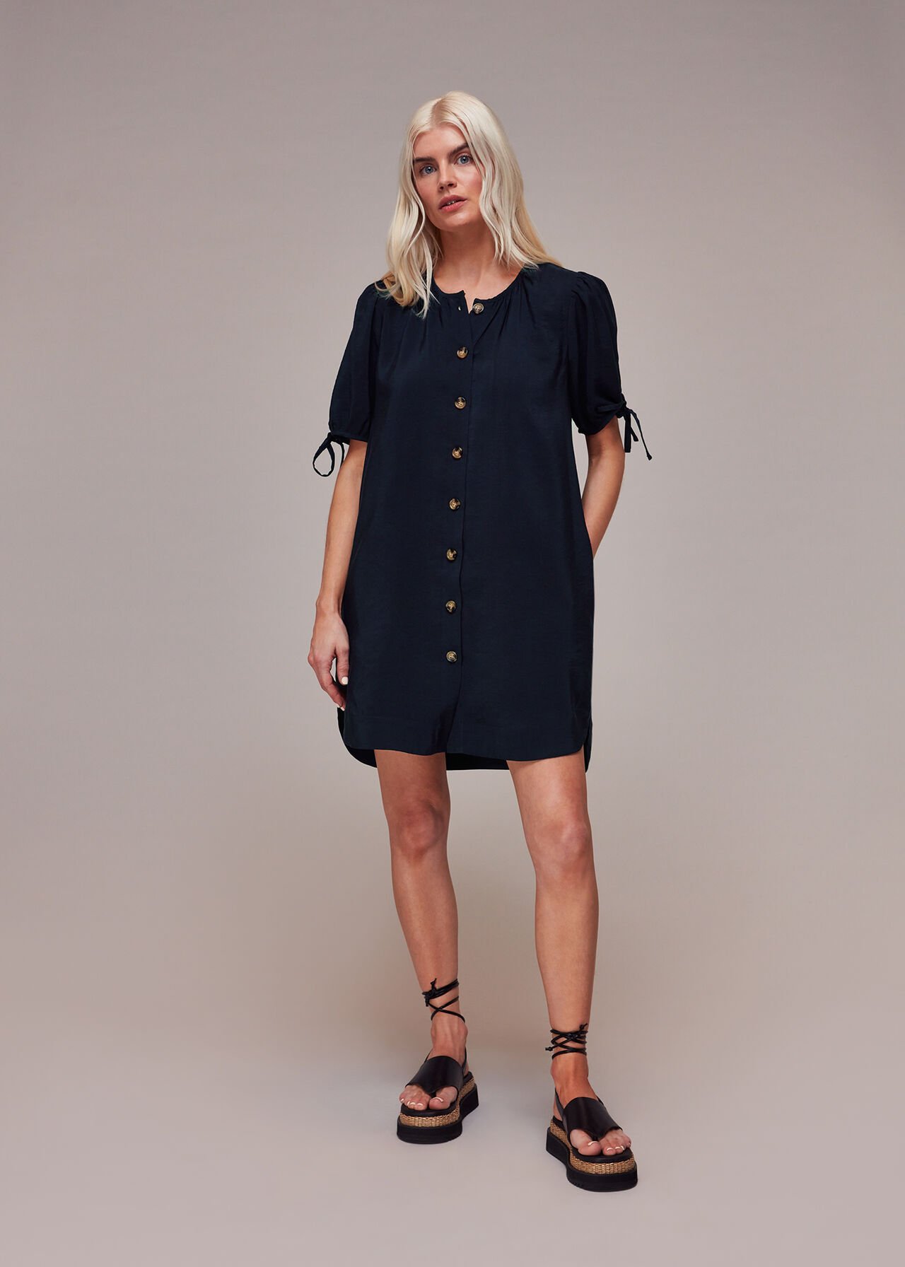 A woman wearing a navy blue button-through dress with short puff sleeves tied at the ends, standing against a plain background.