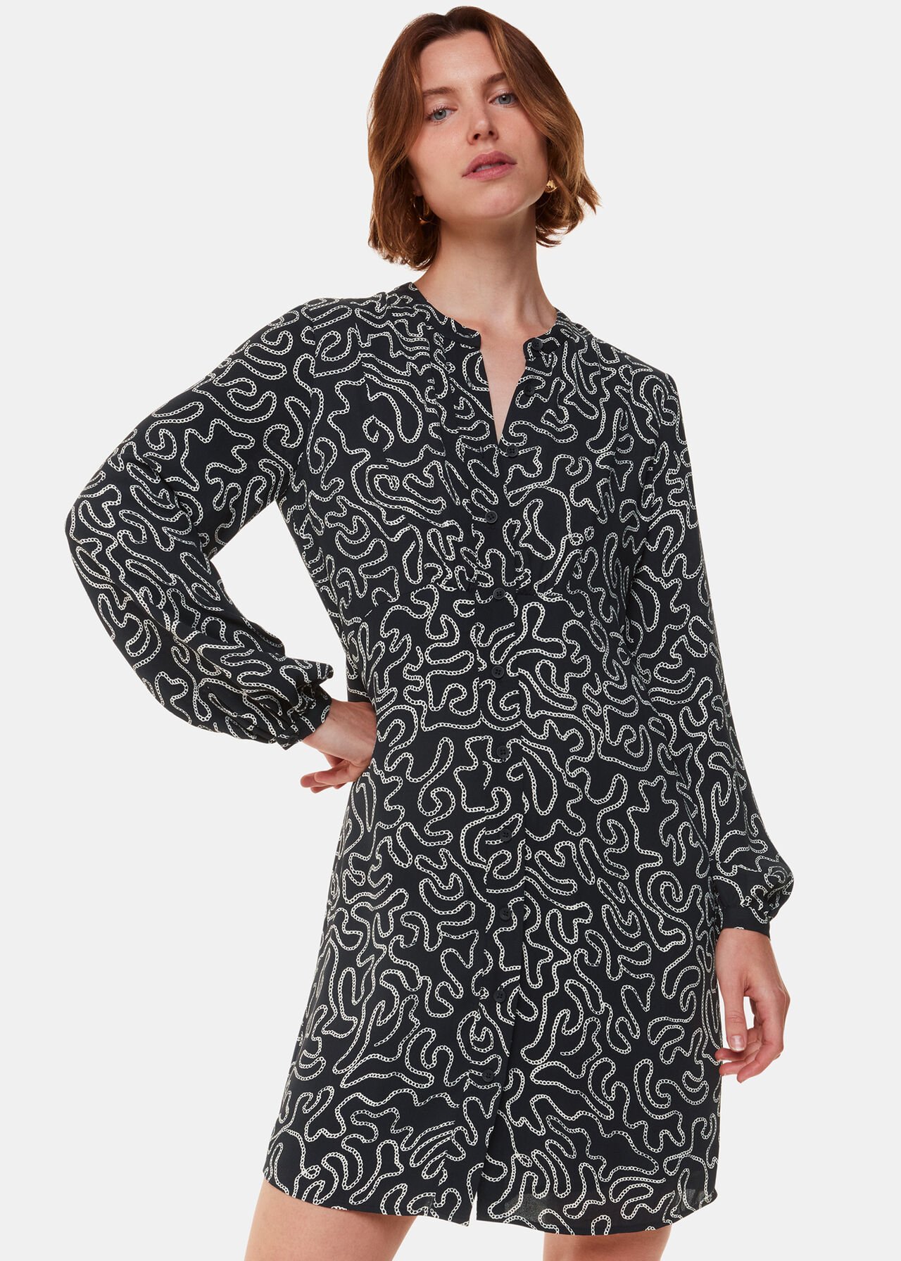 A woman wearing a black dress with a white chain print, long sleeves, and a button-down front.