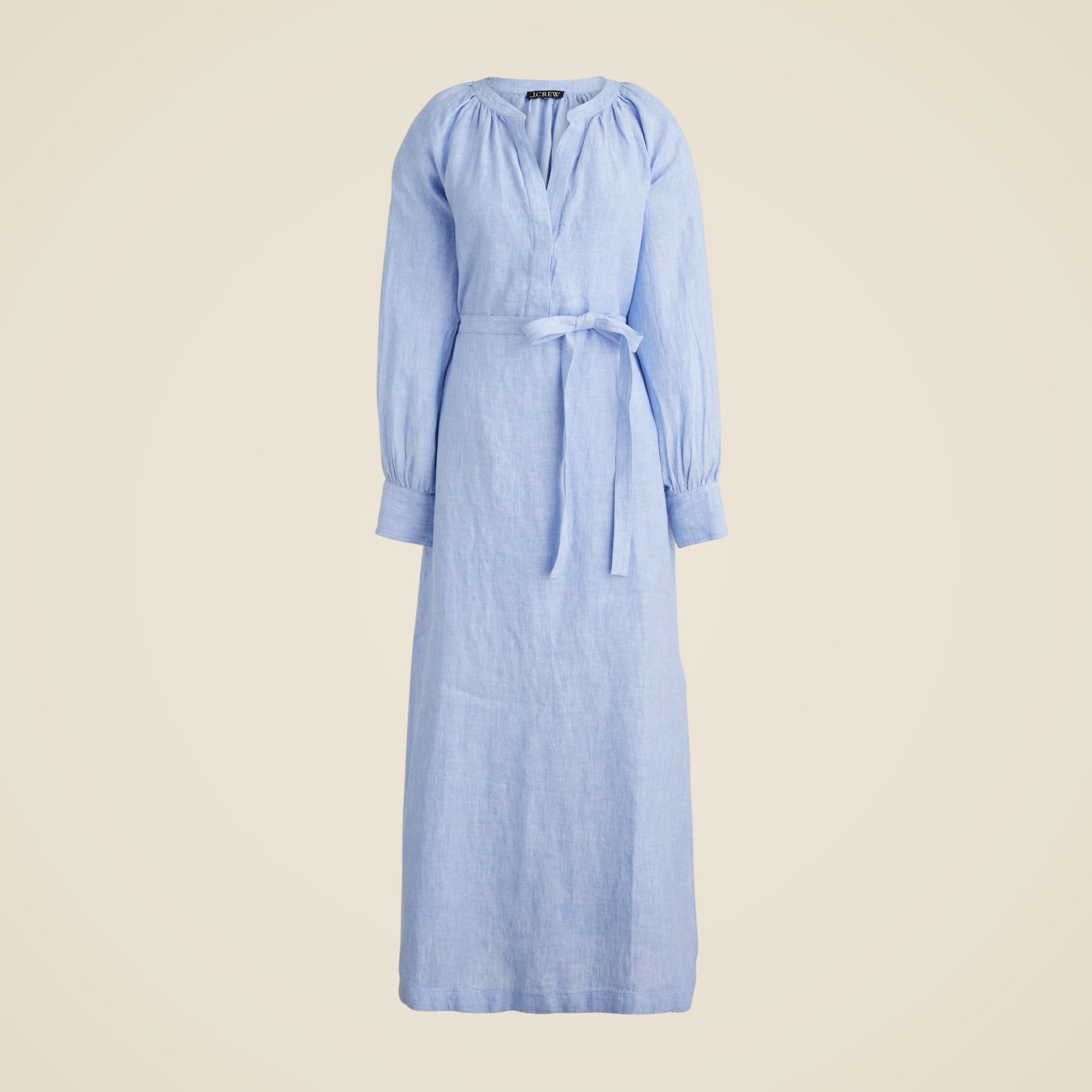 A light blue linen dress with long sleeves, a V neckline, a waist tie, gathered details, and pockets.
