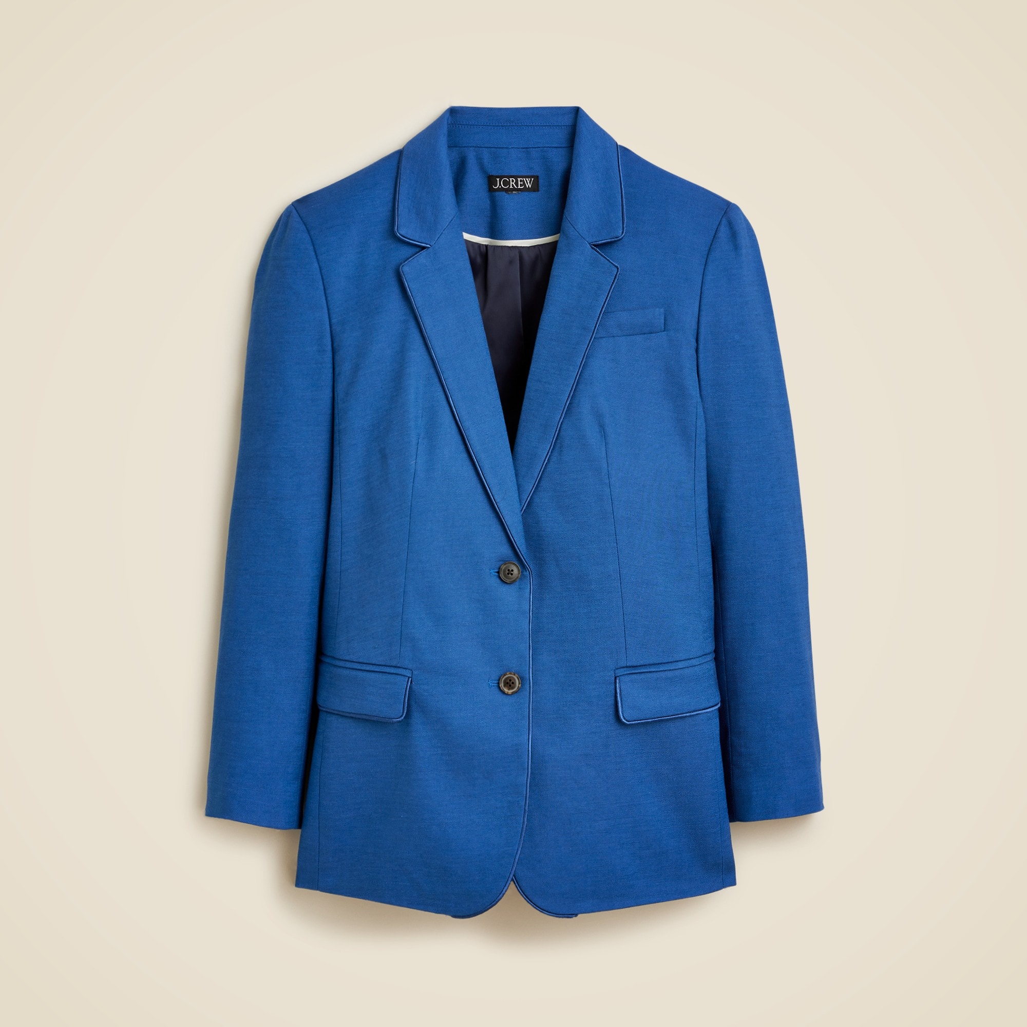 A women's blue blazer with piping details, notch lapel, long sleeves, welt pockets with flaps, and lining.