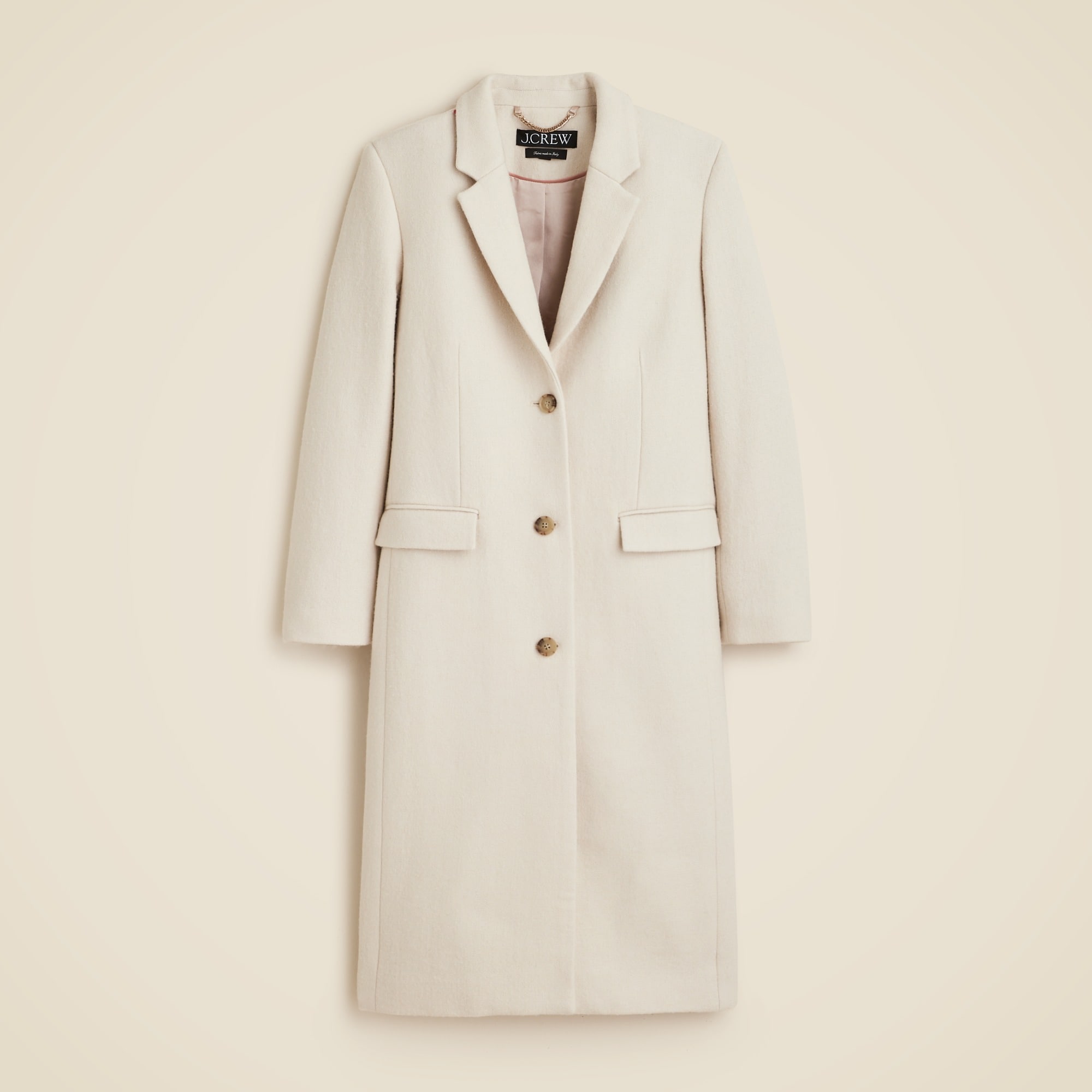 A cream-colored women's topcoat with notch lapels, button closure, flap welt pockets, and a long hem, made from Italian wool-blend melton fabric.