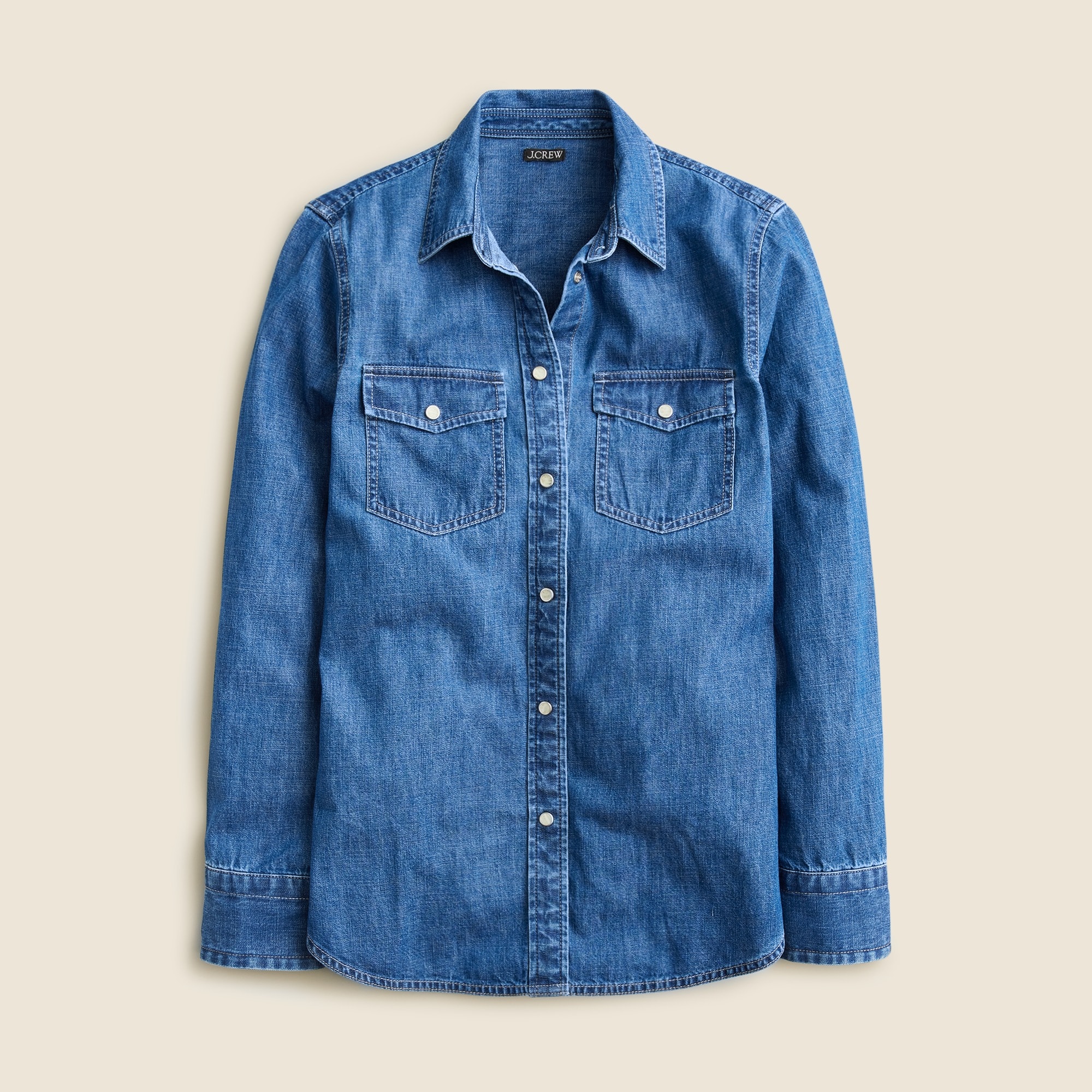 A women's blue chambray shirt with a slim fit, featuring chest pockets with flaps, contrast stitching, snap buttons, and a classic collar.