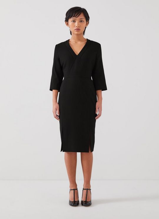 A woman wearing a black petite crepe dress with a deep V-neck, three-quarter sleeves, and a slit on the pencil skirt.