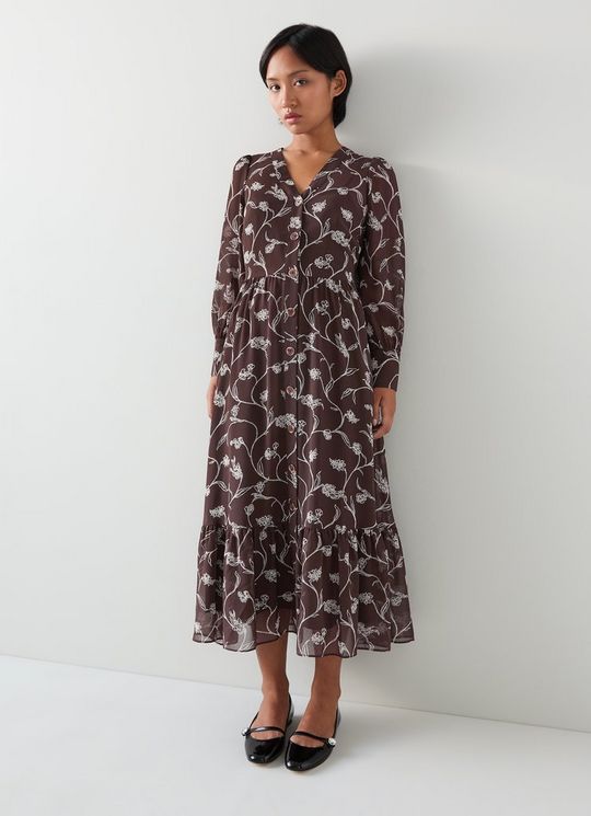 A woman wearing a long, tiered floral dress with a V-neckline and full-length sleeves in chocolate and birch colors.