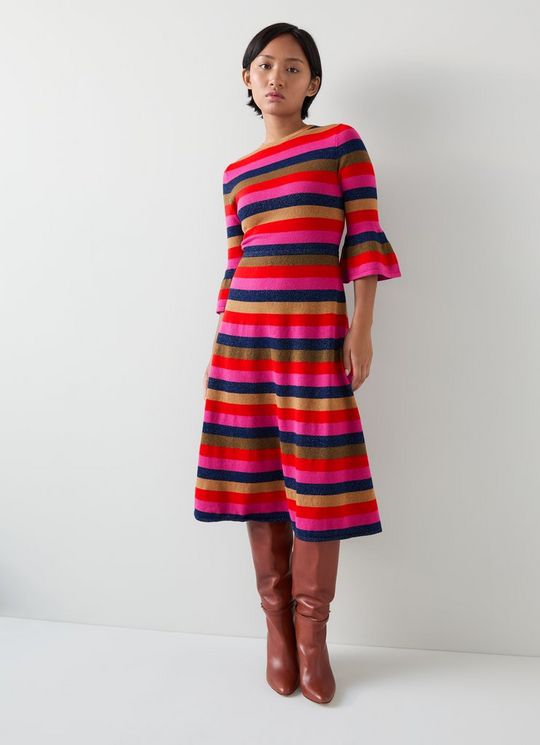 A woman wearing a colorful striped dress with frill hem, crew neck, and full-length sleeves, paired with brown knee-high boots.