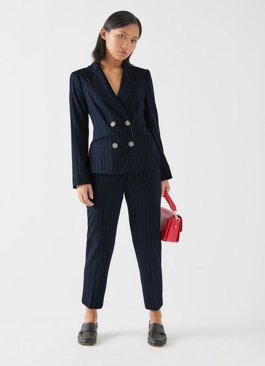 A woman wearing a navy blue pinstripe wool blazer with double-breasted style and horn buttons, paired with matching pinstripe trousers, holding a red handbag.