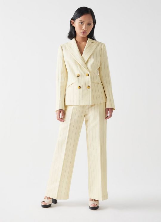 A woman wearing a cream and black pinstripe tailored jacket with a double-breasted style and faux horn buttons, paired with matching cream and black pinstripe trousers.
