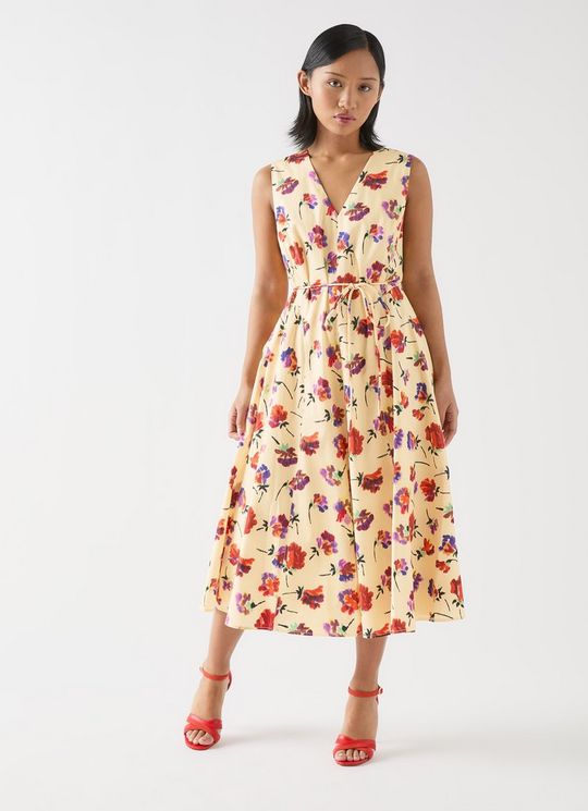 A woman wearing a sleeveless, floral print midi dress with a full skirt and a rouleau belt, standing against a plain background.