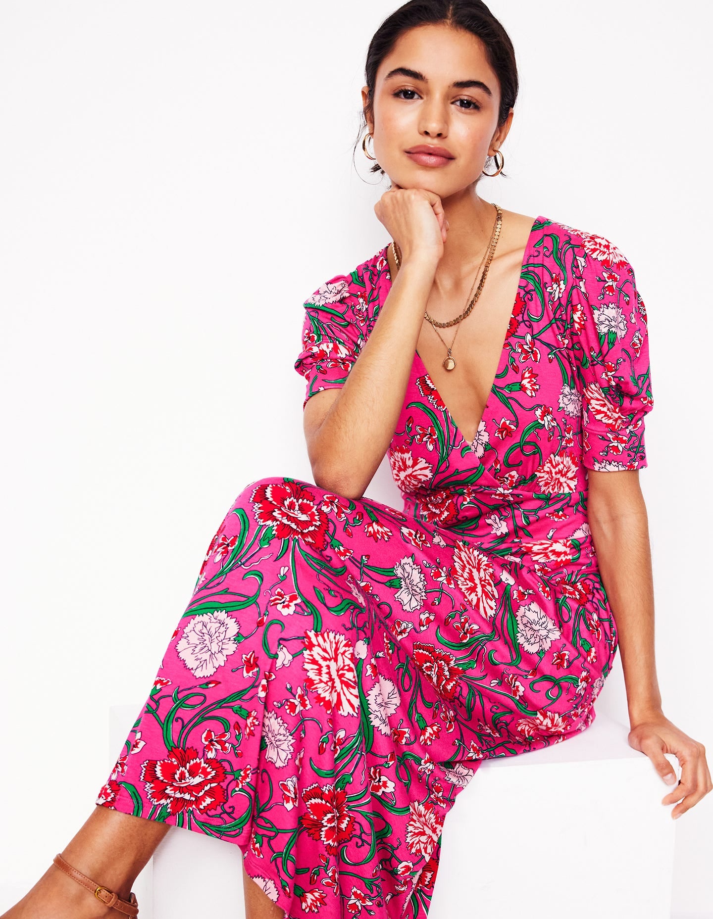 A woman wearing a pink floral dress with a V-neckline, pleated fabric, and a fit and flare silhouette.