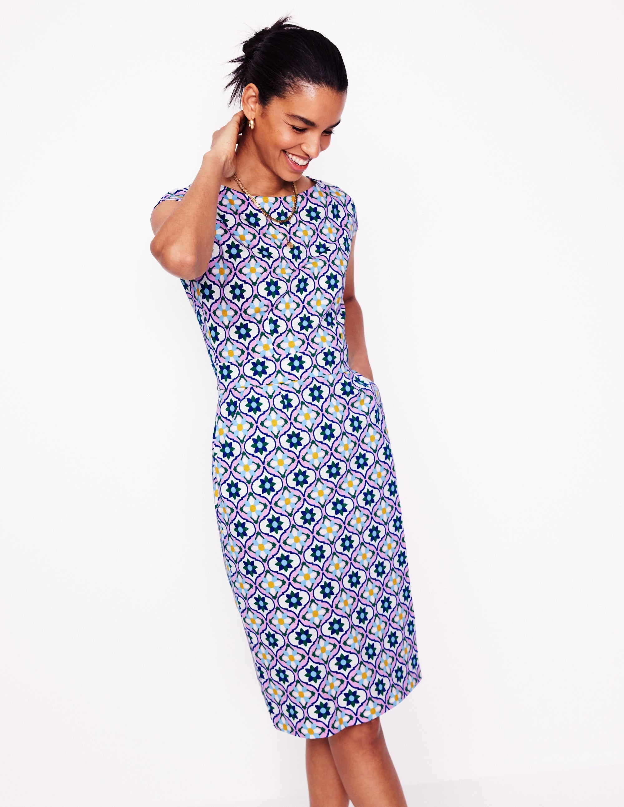 A woman wearing a knee-length dress with a colorful floweret tile pattern, long sleeves, and side pockets, made from jersey fabric.