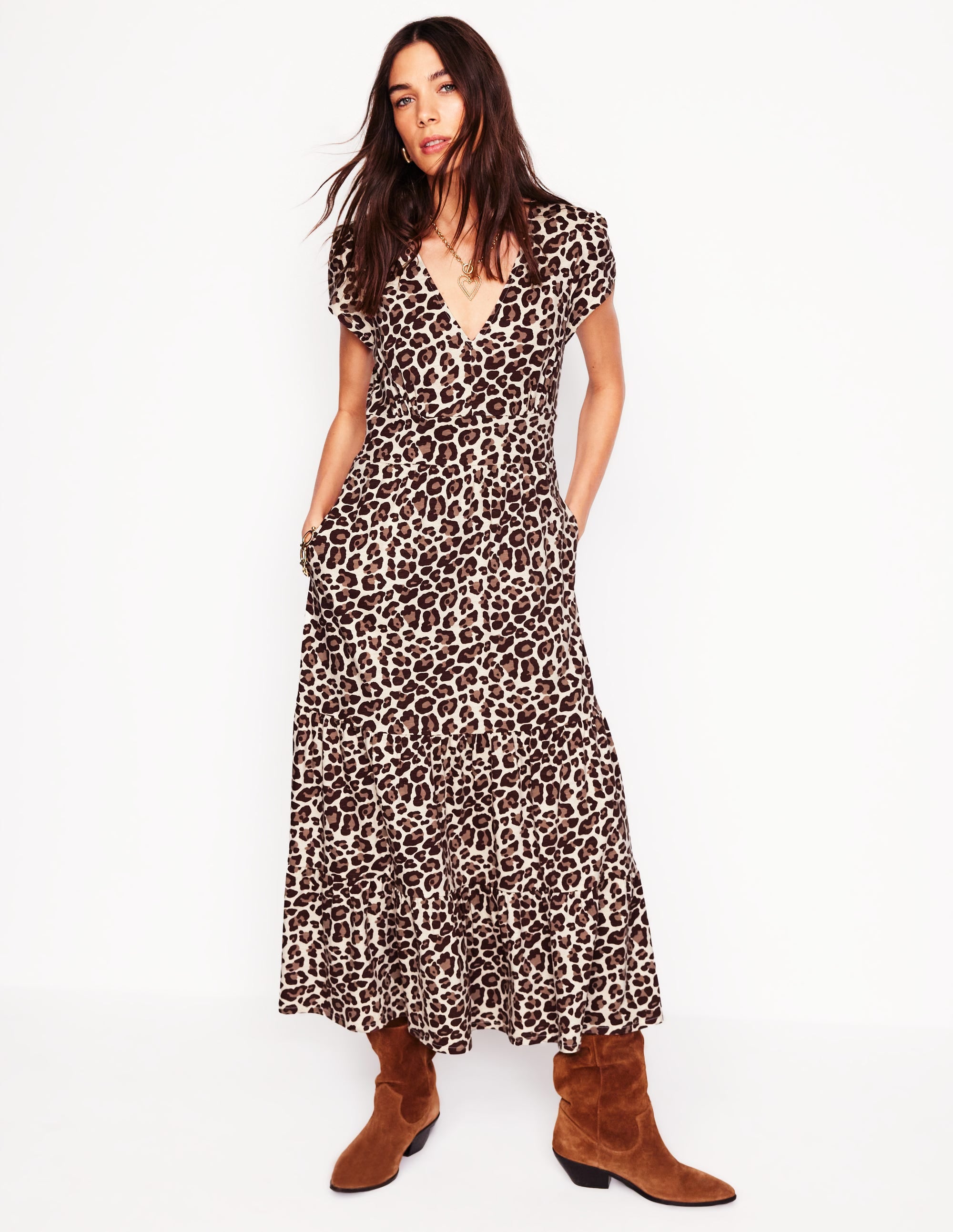 A woman wearing a cheetah print tiered midi dress with side pockets and cap sleeves, paired with brown boots.