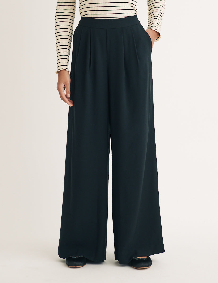 A pair of black wide-leg trousers with a pleated front and elasticated waistband, styled with a striped top.