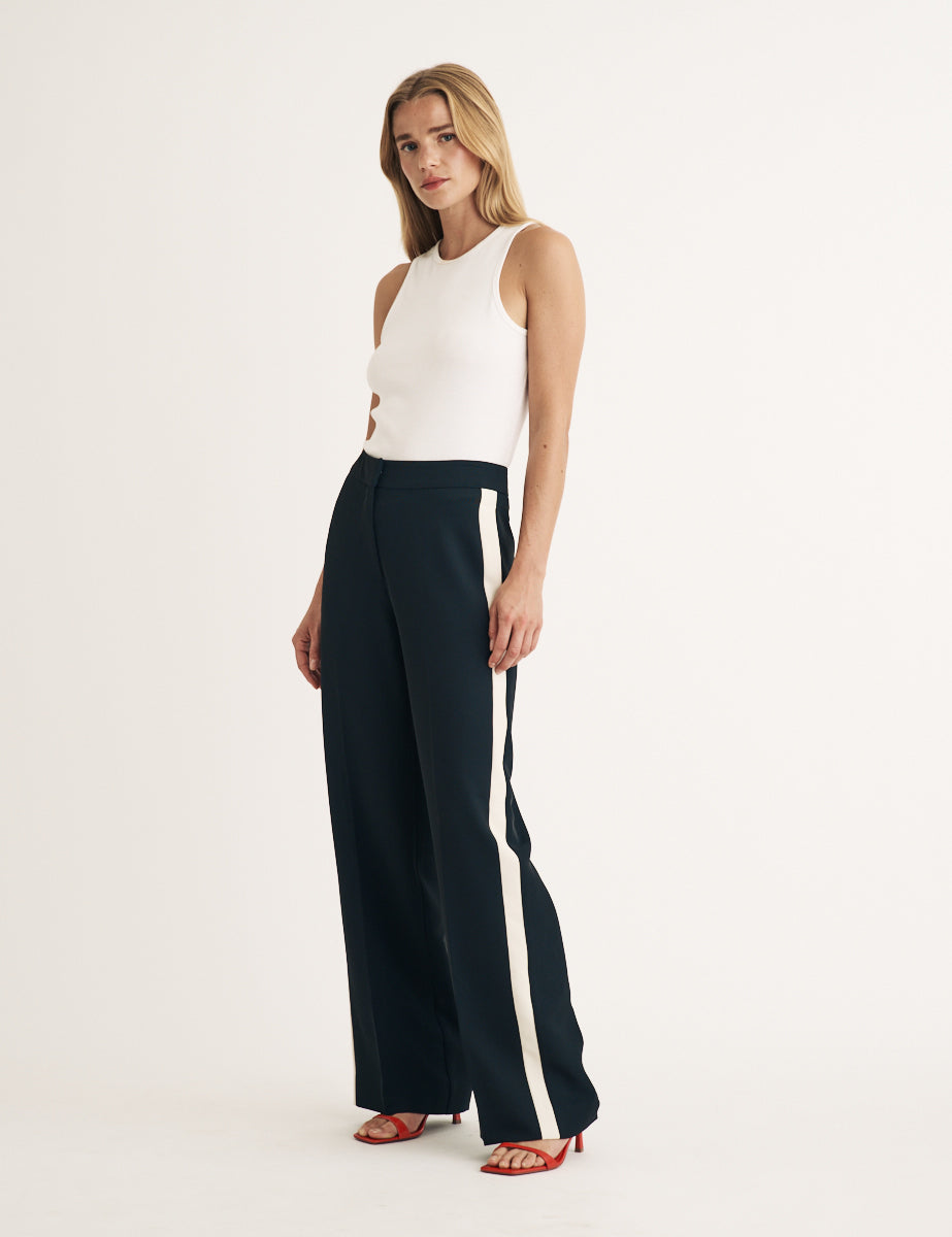 A woman wearing black high-waisted trousers with a side stripe, paired with a white sleeveless top and red heels.