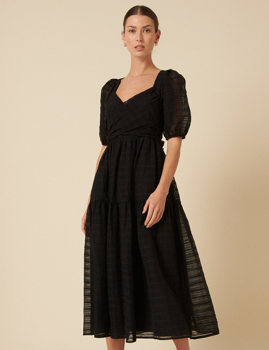 A woman wearing a black midi dress with puff sleeves, a sweetheart neckline, and a relaxed skirt, made from organza fabric.