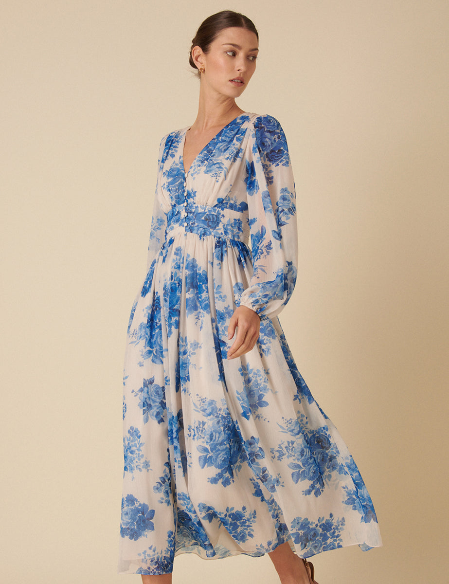 A woman wearing a blue and white floral midi dress with puff sleeves, a fitted waist, and fabric-covered buttons, made from recycled polyester.