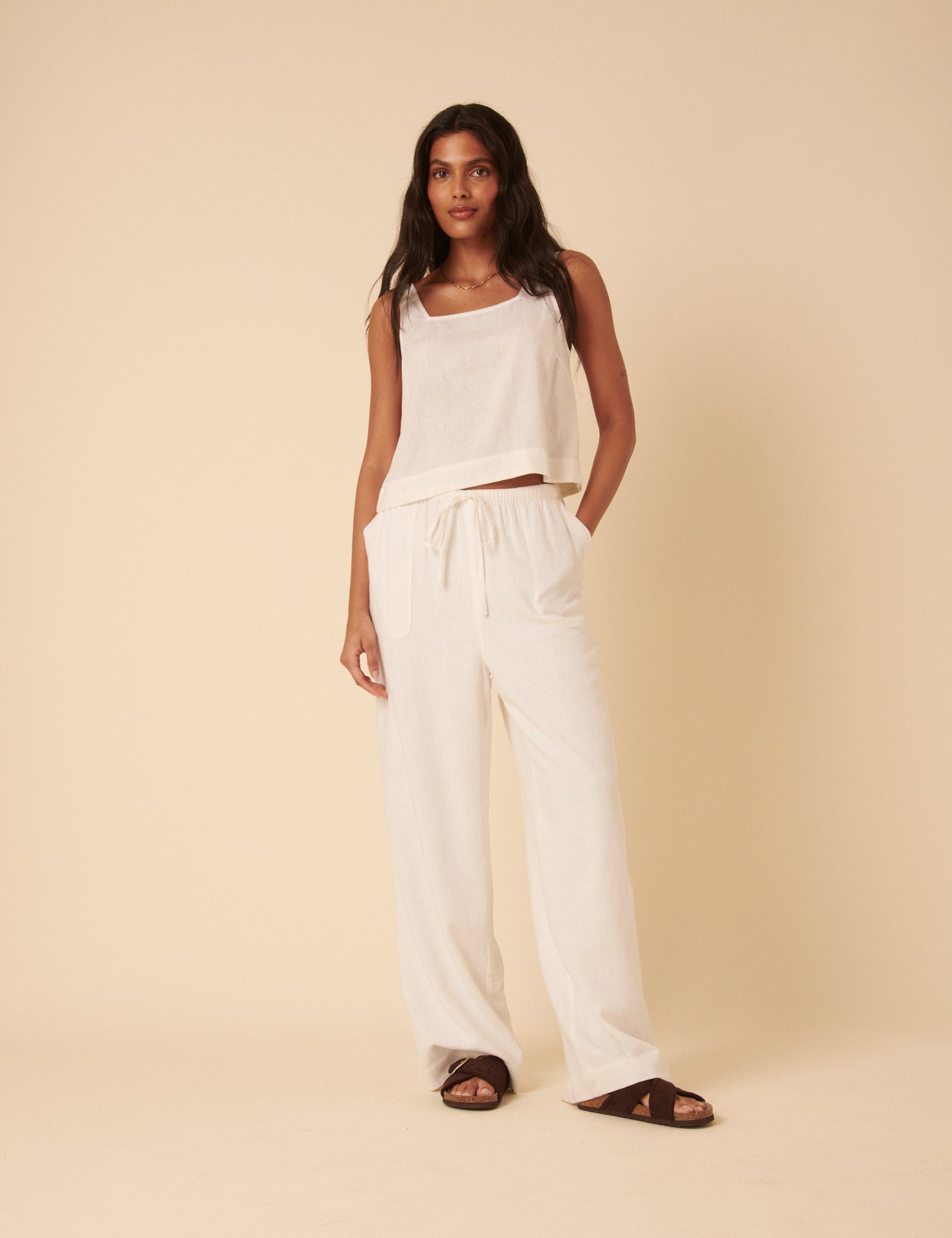 A woman wearing white linen-blend Shona trousers with a wide-leg cut, drawstring waist, and large pockets, paired with a sleeveless top.