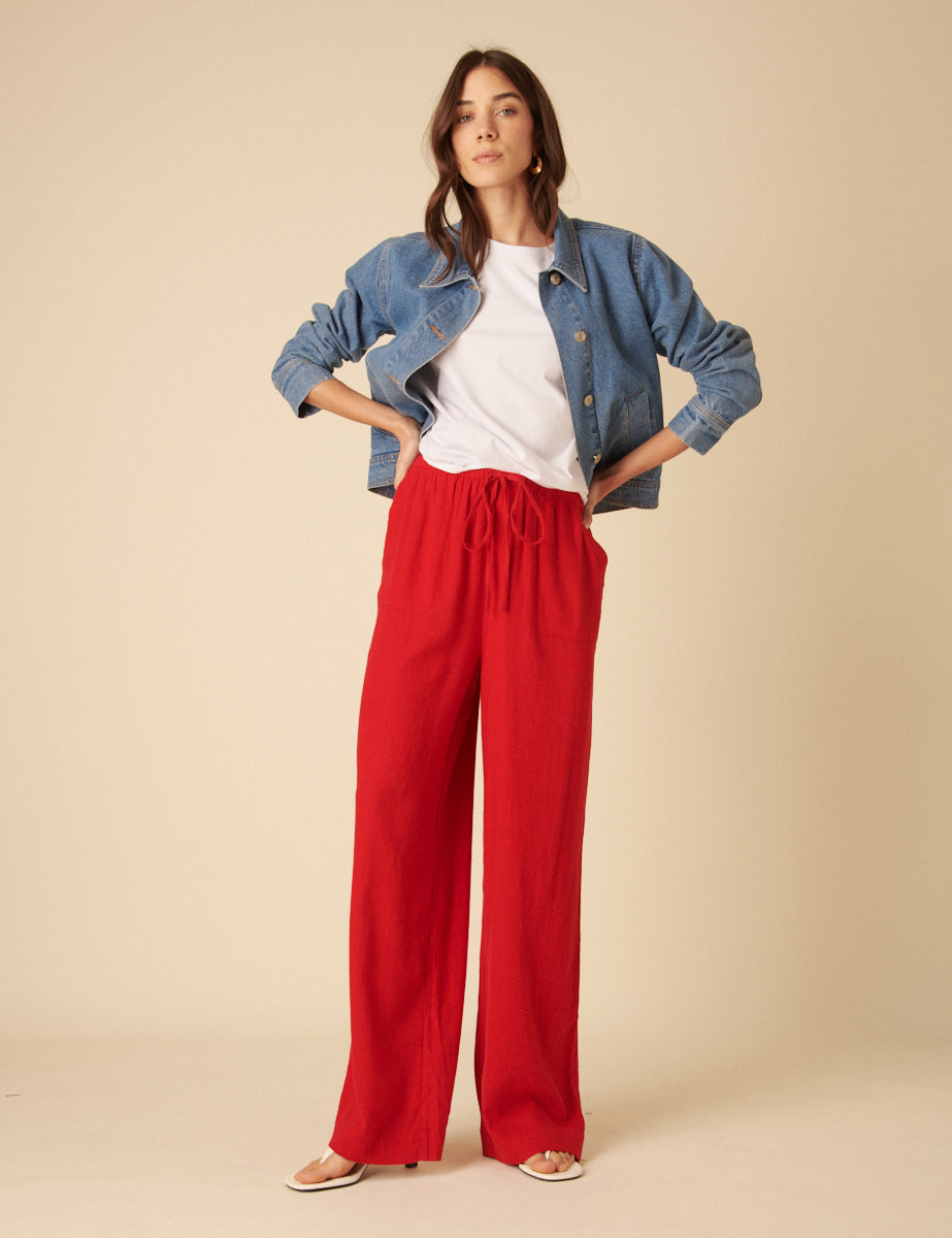 A woman wearing bright red wide-leg trousers with a drawstring waist and side pockets, paired with a white t-shirt and a denim jacket.