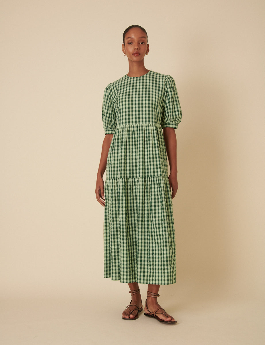 A woman wearing a green gingham midi dress with puffed short sleeves and a tiered design.