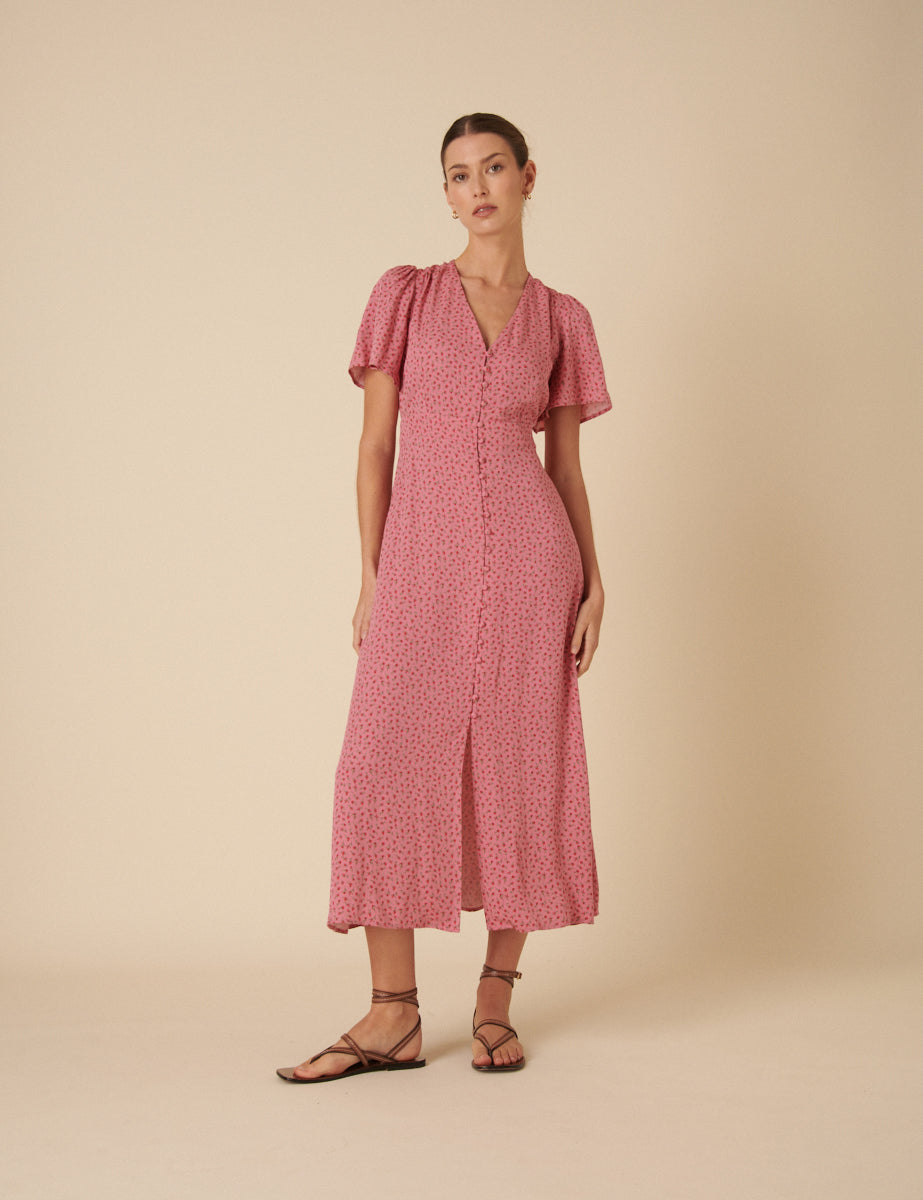 A woman wearing a pink floral printed midi dress with a V-neckline and short puffed sleeves, standing against a beige background.