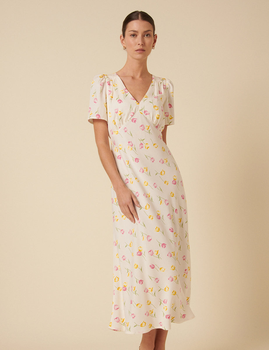 A woman wearing a cream floral printed midi dress with short puff sleeves and a V-neckline.