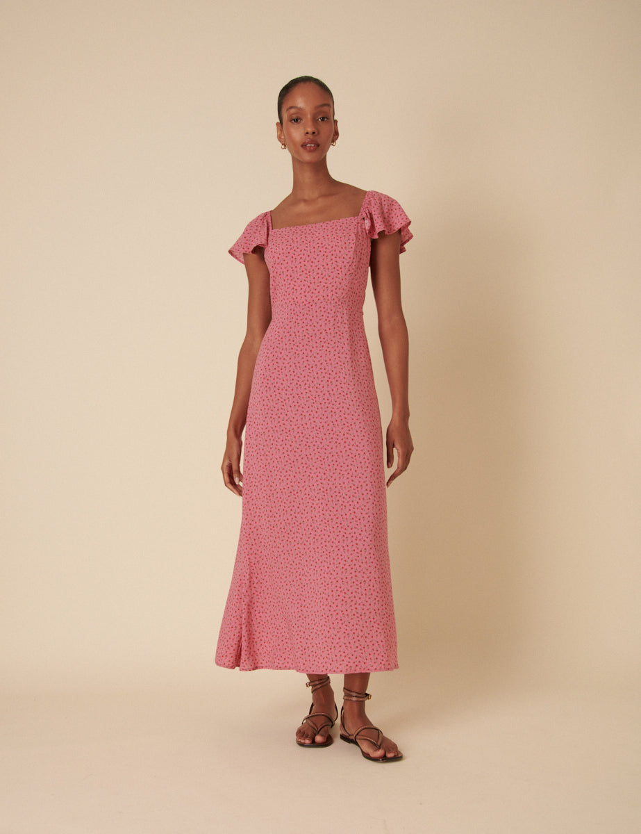 A woman wearing a pink floral midi dress with square neckline, flutter sleeves, and a back waist tie, standing against a plain background.