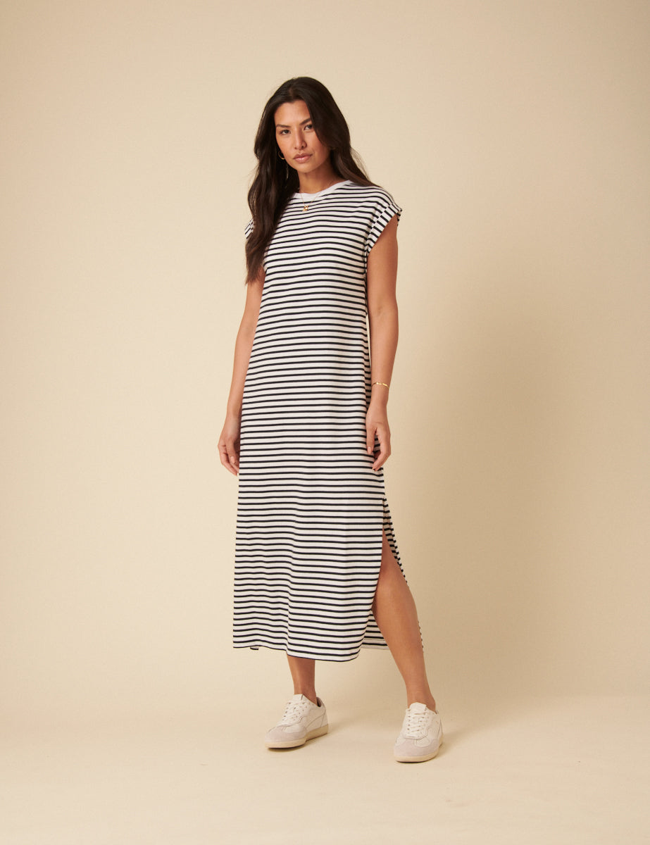 A woman wearing a white and blue striped midi T-shirt dress with a crew neck, short sleeves, and a side slit, paired with white sneakers.
