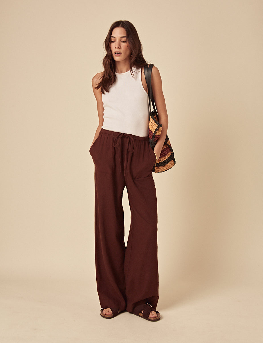 A woman wearing brown wide-leg trousers with a drawstring waist and oversized pockets, paired with a sleeveless white top.