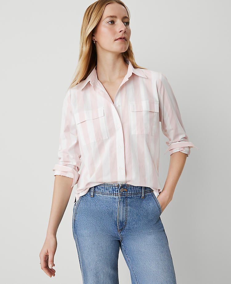 A woman wearing a pink and white striped blouse with long sleeves, chest pockets, and a collar, paired with blue jeans.