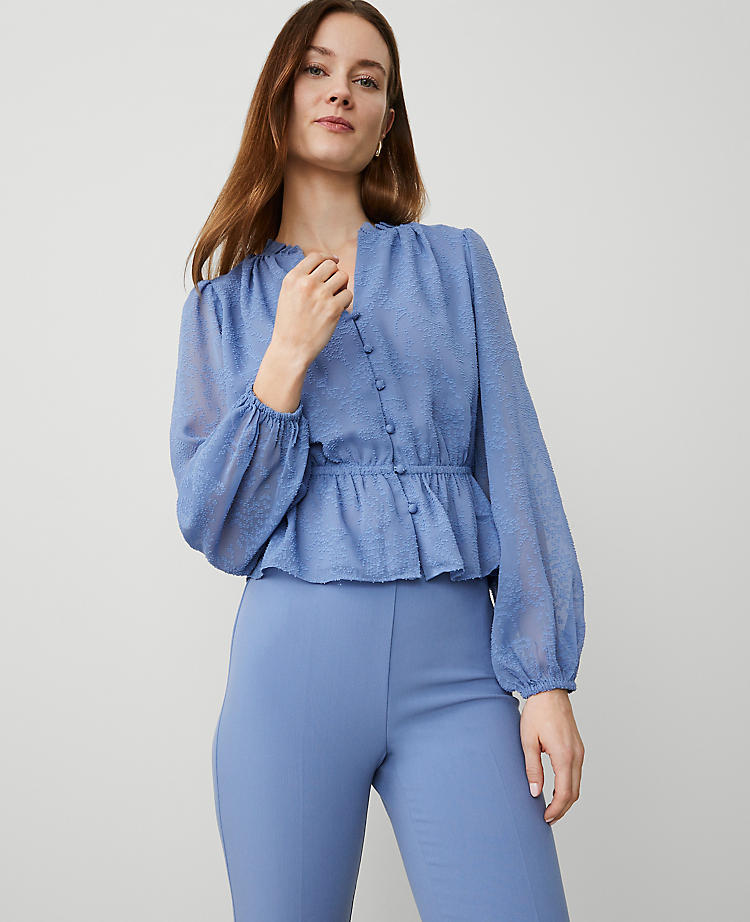 A woman wearing a light blue chiffon blouse with a ruffle collar, puff sleeves, and elasticized waist, paired with matching blue pants.