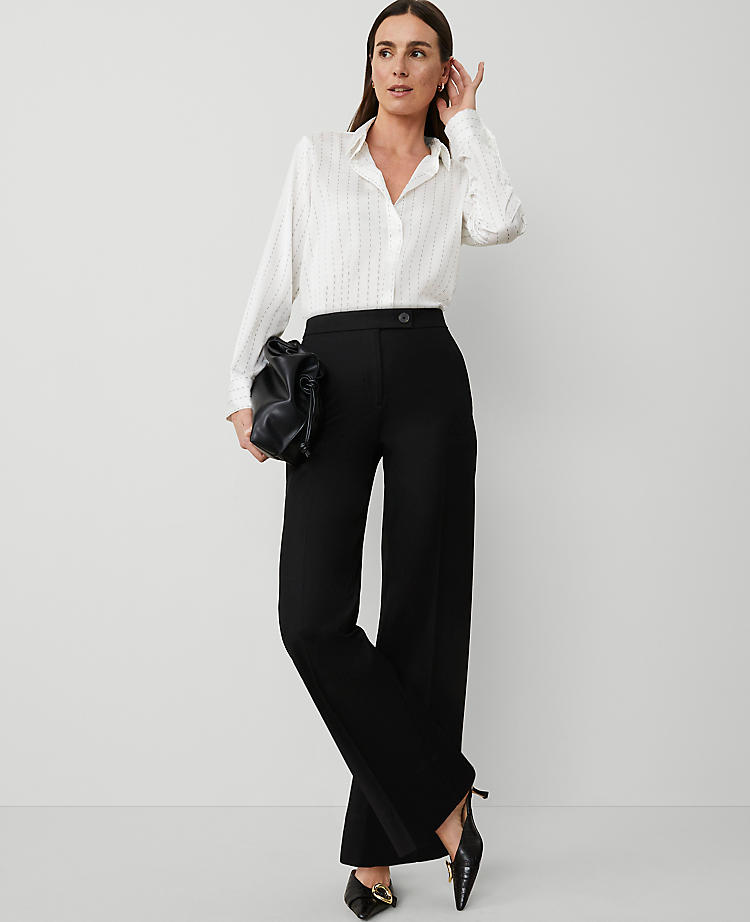 A woman wearing black wide-leg pants with a high waist, front zip, slash pockets, and back flap pockets, paired with a white blouse and black heels.