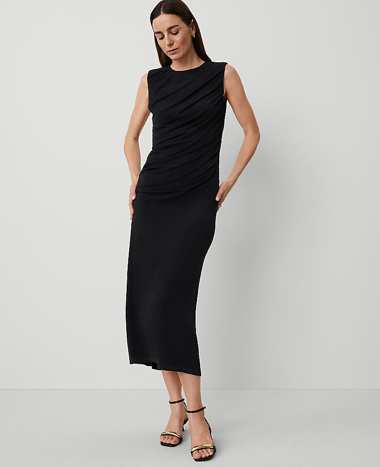 A woman wearing a black sleeveless knit midi sheath dress with a round neckline and back-zip closure, paired with black high-heeled sandals.