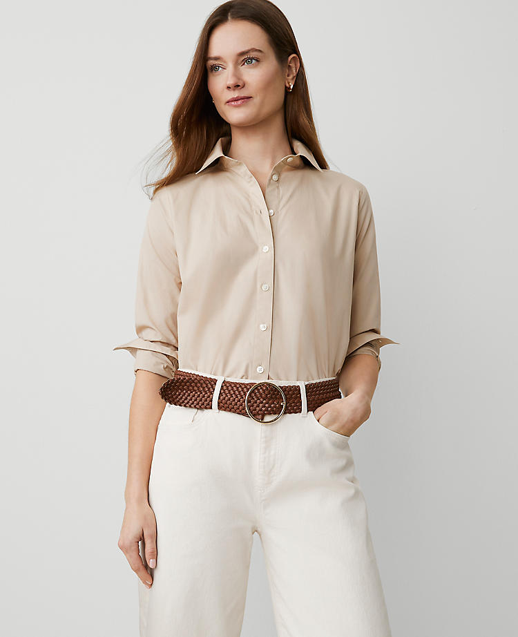 A woman wearing a beige relaxed-fit cotton shirt with a point collar, button-down front, long sleeves with button cuffs, and a shirttail hem.