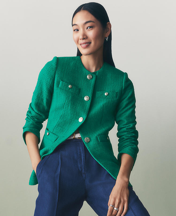 A woman wearing a vibrant green petite tweed split hem jacket with silver buttons, long sleeves, and welt pockets, styled with blue pants.