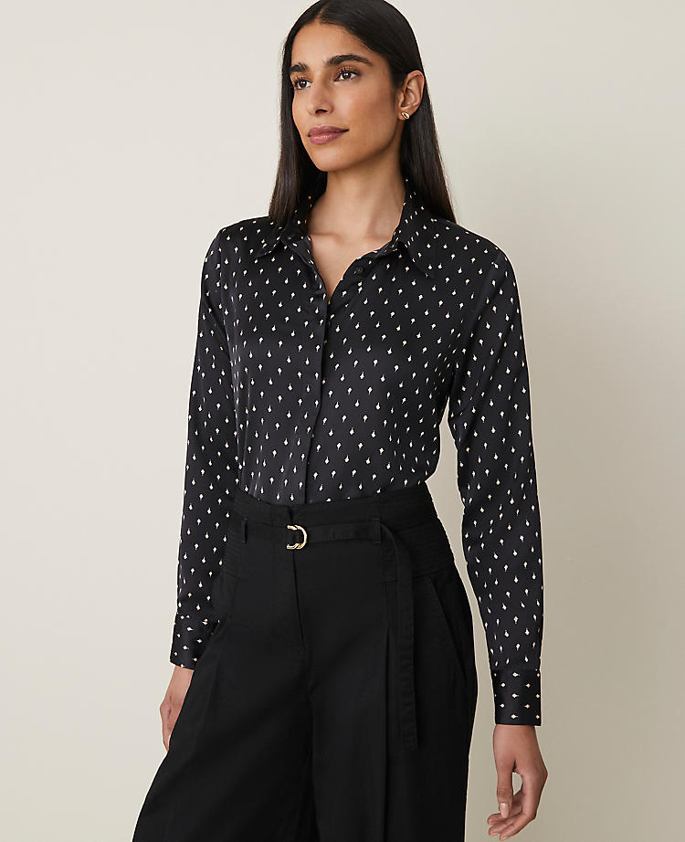 A woman wearing a black dotted shirt with a point collar and long sleeves, paired with black trousers.